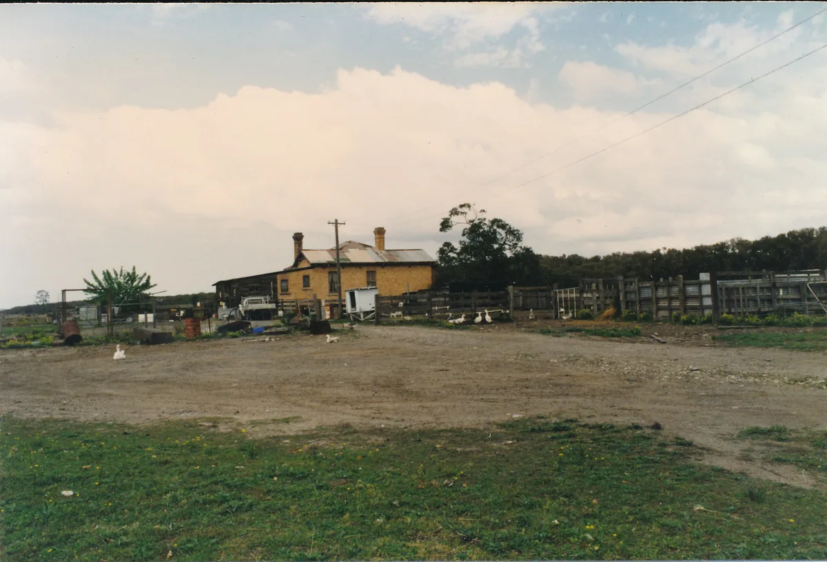 The house before restoration, seen across a bare farmyard with duck pens and sheds