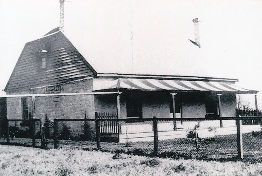 Black and white photograph of an island farmhouse with a striped verandah awning and picket fence